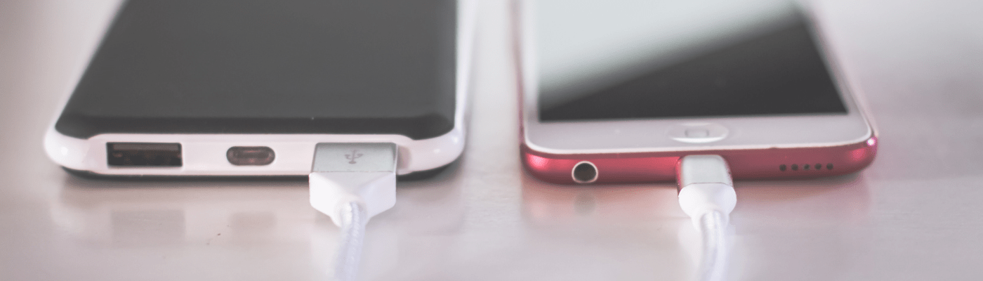 Photo of a phone and external battery sitting side-by-side on a table. They are connected by a charging cord.
